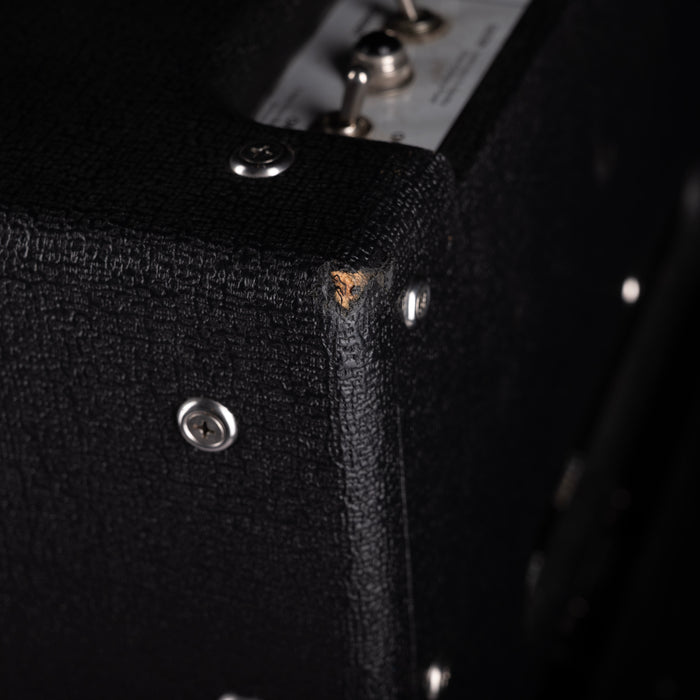 Close-up of a black guitar amplifier with visible screws and text.