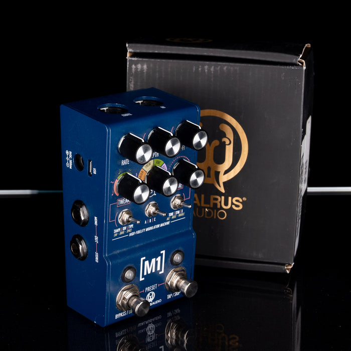Blue guitar effects pedal with a black box featuring a brand logo on a reflective surface.