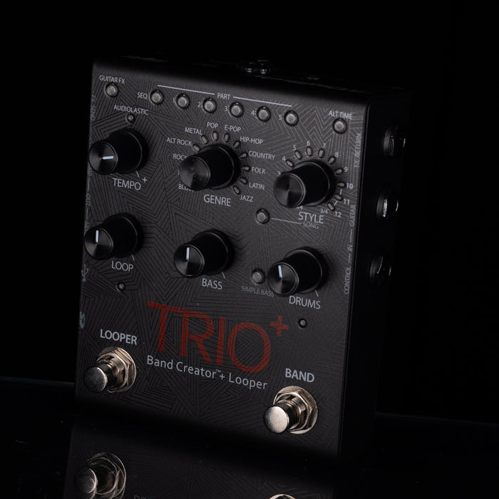 A close-up of a black Trio Band Creator+ Looper guitar effects pedal with multiple rotary knobs, switches, and foot pedals against a dark background.