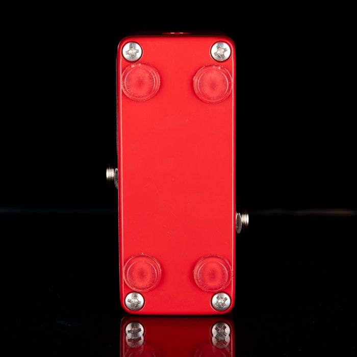Red guitar effects pedal with four screws on a black background