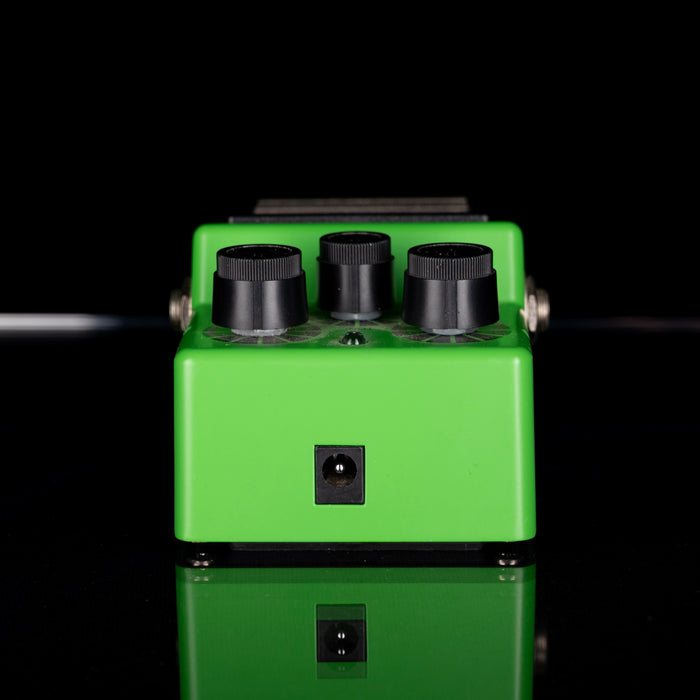 Green guitar effects pedal with black knobs on a reflective surface