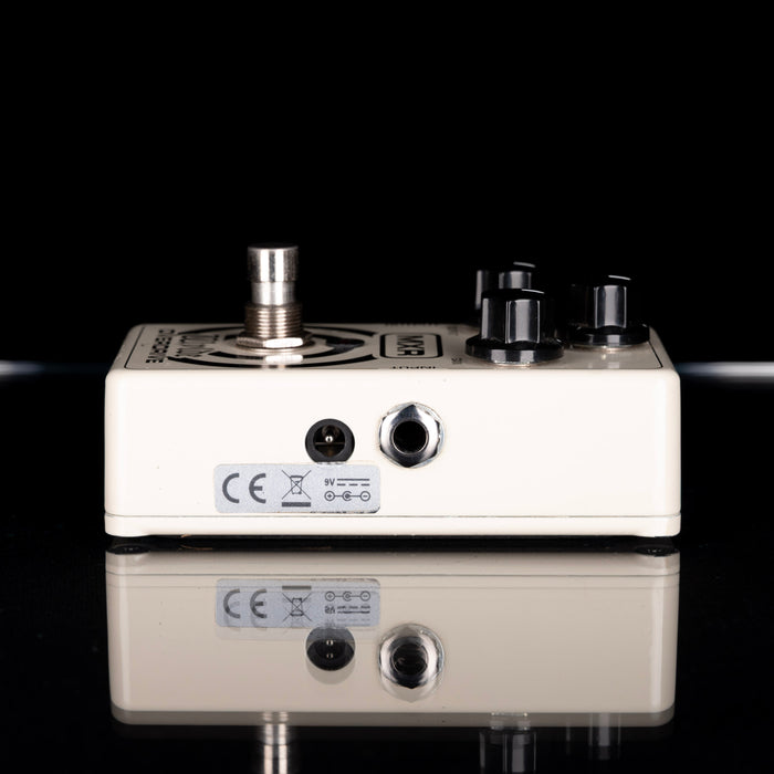 Guitar effects pedal with control knobs and connectors on a reflective surface.