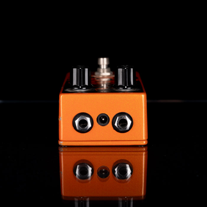 Orange guitar effects pedal with metallic knobs on a black background
