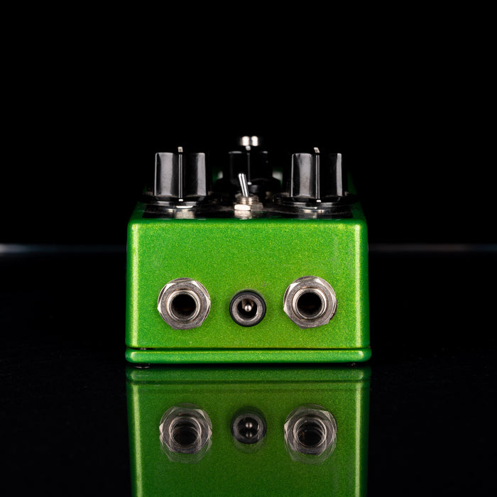 Green guitar effects pedal with multiple knobs on a black background