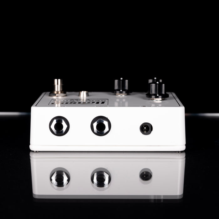 White guitar effects pedal with black knobs on a reflective surface with black background