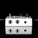 White guitar effects pedal with black knobs on a reflective surface with black background
