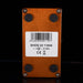 The back of a copper-colored guitar effects pedal with four black rubber feet and a white barcode label in the center, shown against a black background.