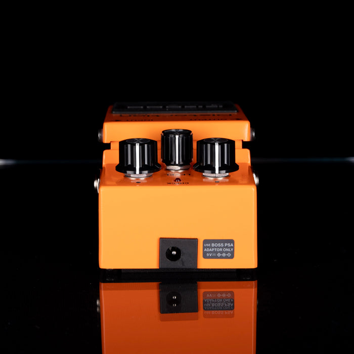 Orange guitar effects pedal with black knobs on a reflective surface.