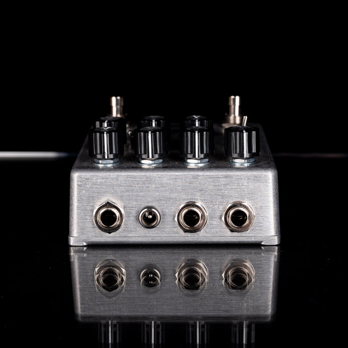 Metallic guitar effects pedal with multiple knobs and ports on a reflective surface.