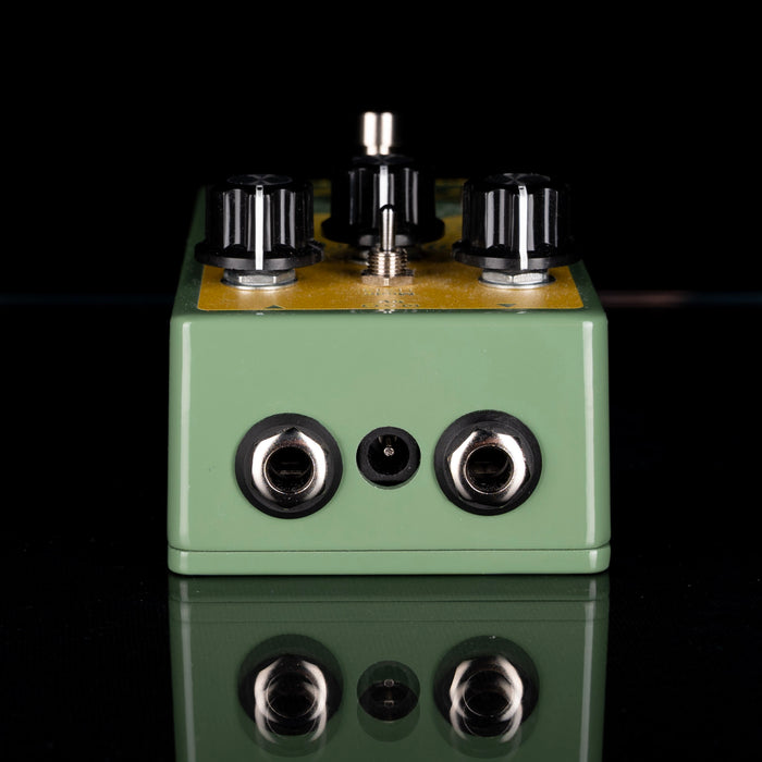 Green guitar effects pedal with knobs and jacks on a reflective surface