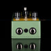 Green guitar effects pedal with knobs and jacks on a reflective surface