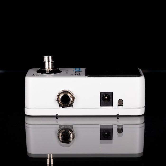 White guitar effects pedal with multiple connectors on a reflective surface.