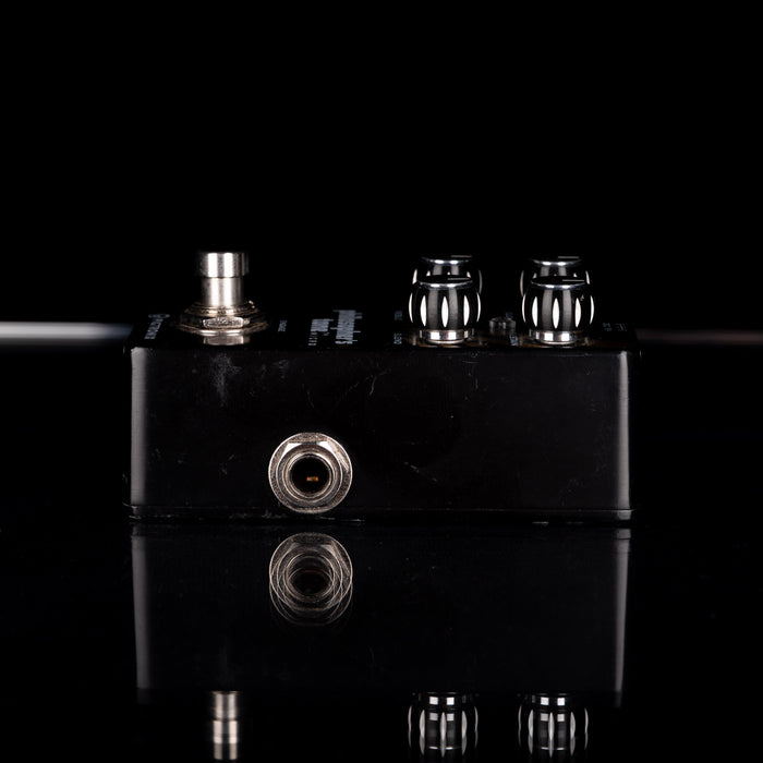 Black guitar effects pedal with metallic knobs on a reflective surface