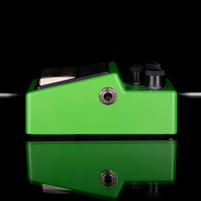 Green guitar effects pedal with black components on a reflective surface