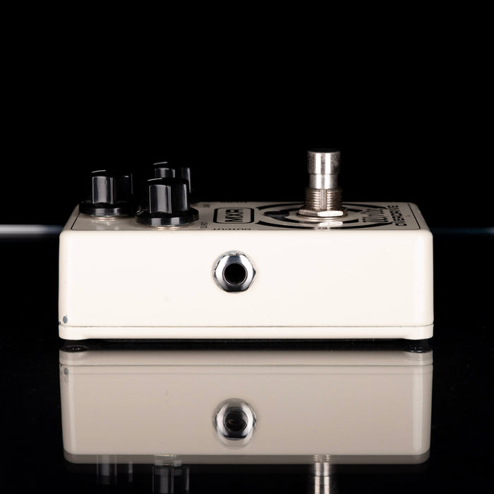 White guitar effects pedal with black knobs on a reflective surface