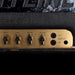 Close-up of a guitar amplifier with control knobs and labels.