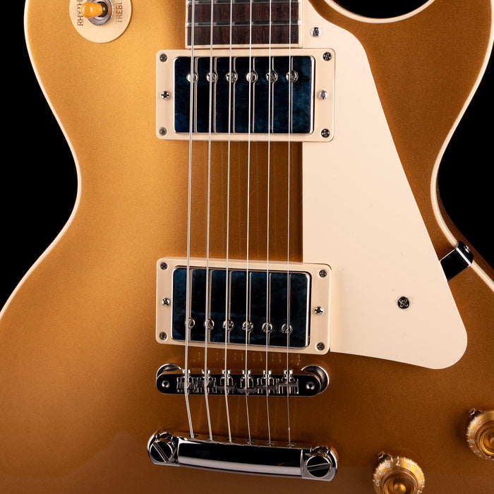 Close-up of a gold electric guitar with a black pickguard on a black background