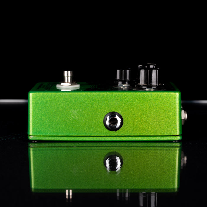 Green guitar effects pedal on a reflective black surface with a black background