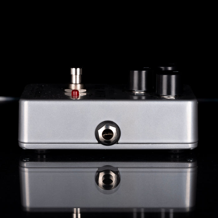 Close-up of a metallic electronic device with knobs and ports on a reflective black surface.