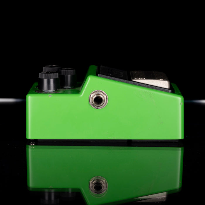Green guitar effects pedal with black knobs on a reflective surface