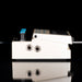 White guitar effects pedal with blue and black knobs on a reflective surface with a black background