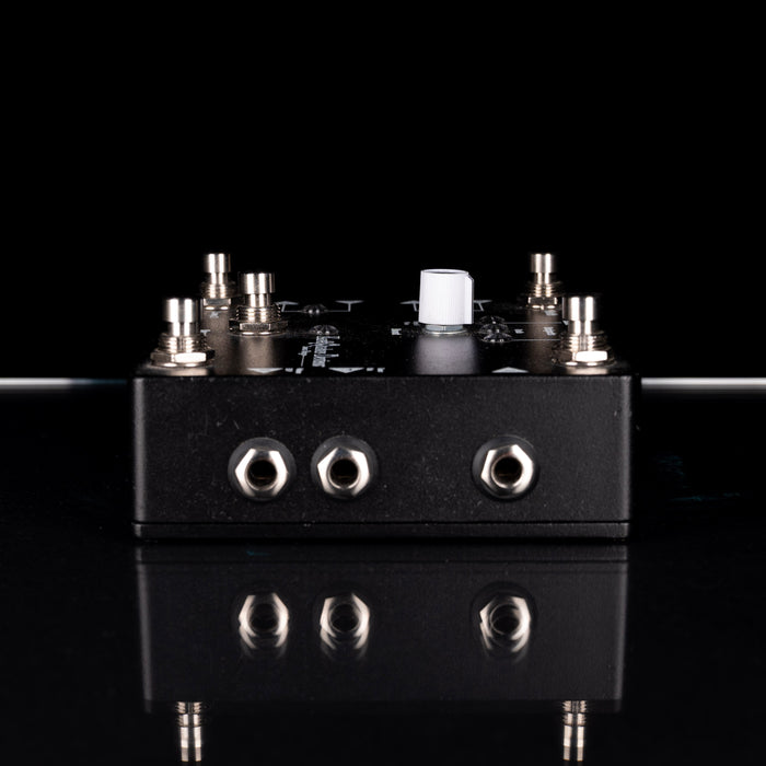 Black guitar effects pedal with multiple jacks on a reflective black surface.