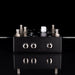Black guitar effects pedal with multiple jacks on a reflective black surface.