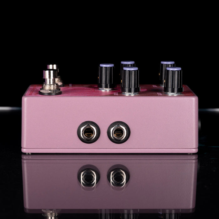 Purple guitar effects pedal with knobs and jacks on a reflective surface