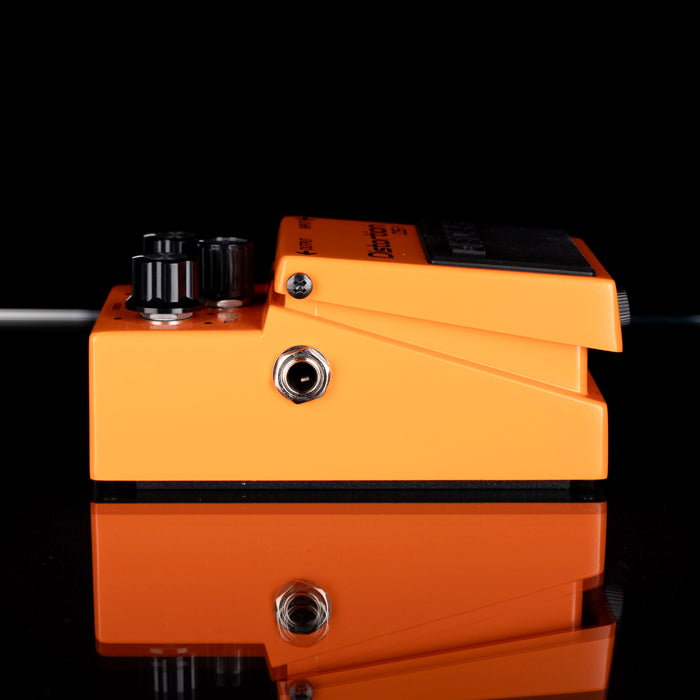 Orange guitar effects pedal with black knobs on a reflective surface