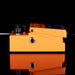 Orange guitar effects pedal with black knobs on a reflective surface