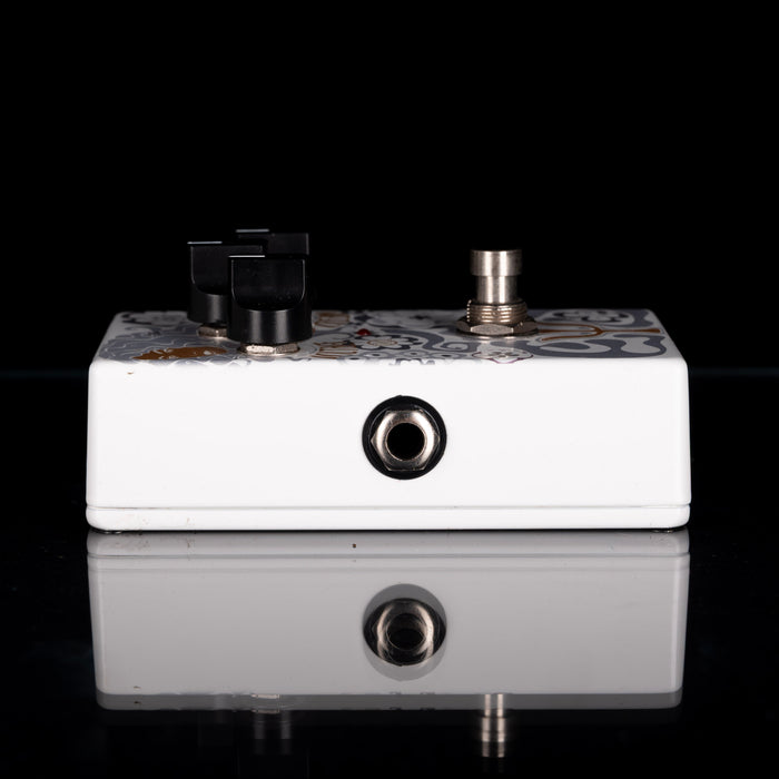 Guitar effects pedal with white casing and decorative top on a black background