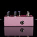 Purple guitar effects pedal with knobs and jacks on a reflective surface